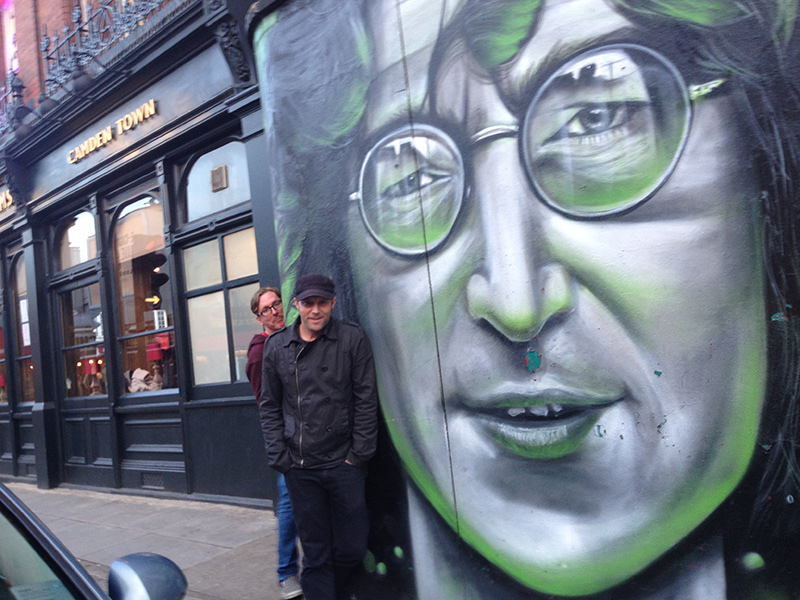 Two men standing by a mural of John Lennon in Camden Town.